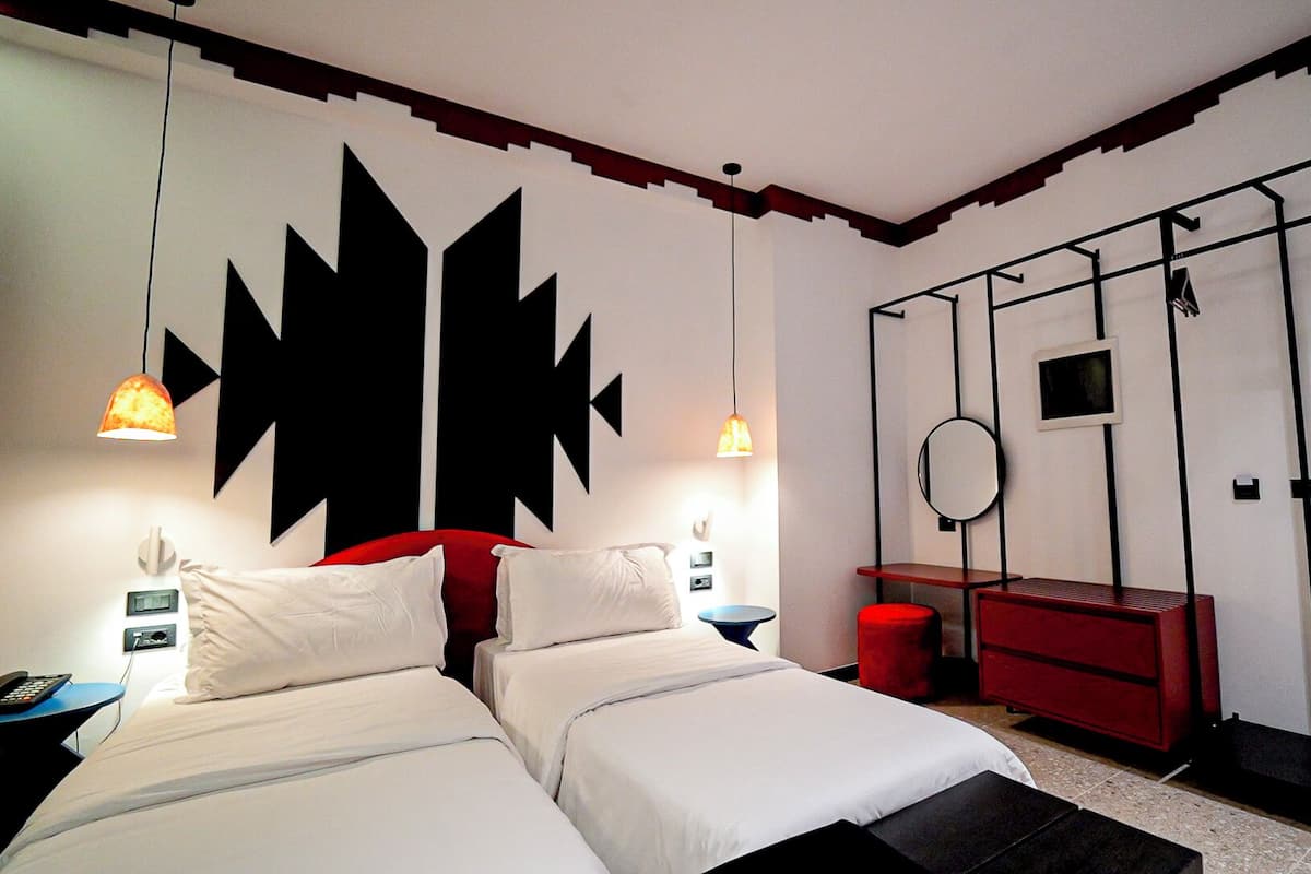 A hotel room with two beds, a red dresser, a mirror, and a large black wall decoration.