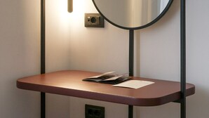 A bathroom with a round mirror mounted on a wall, a wooden vanity, and a light fixture above the mirror. - Bazaar Hotel  (Tirana)