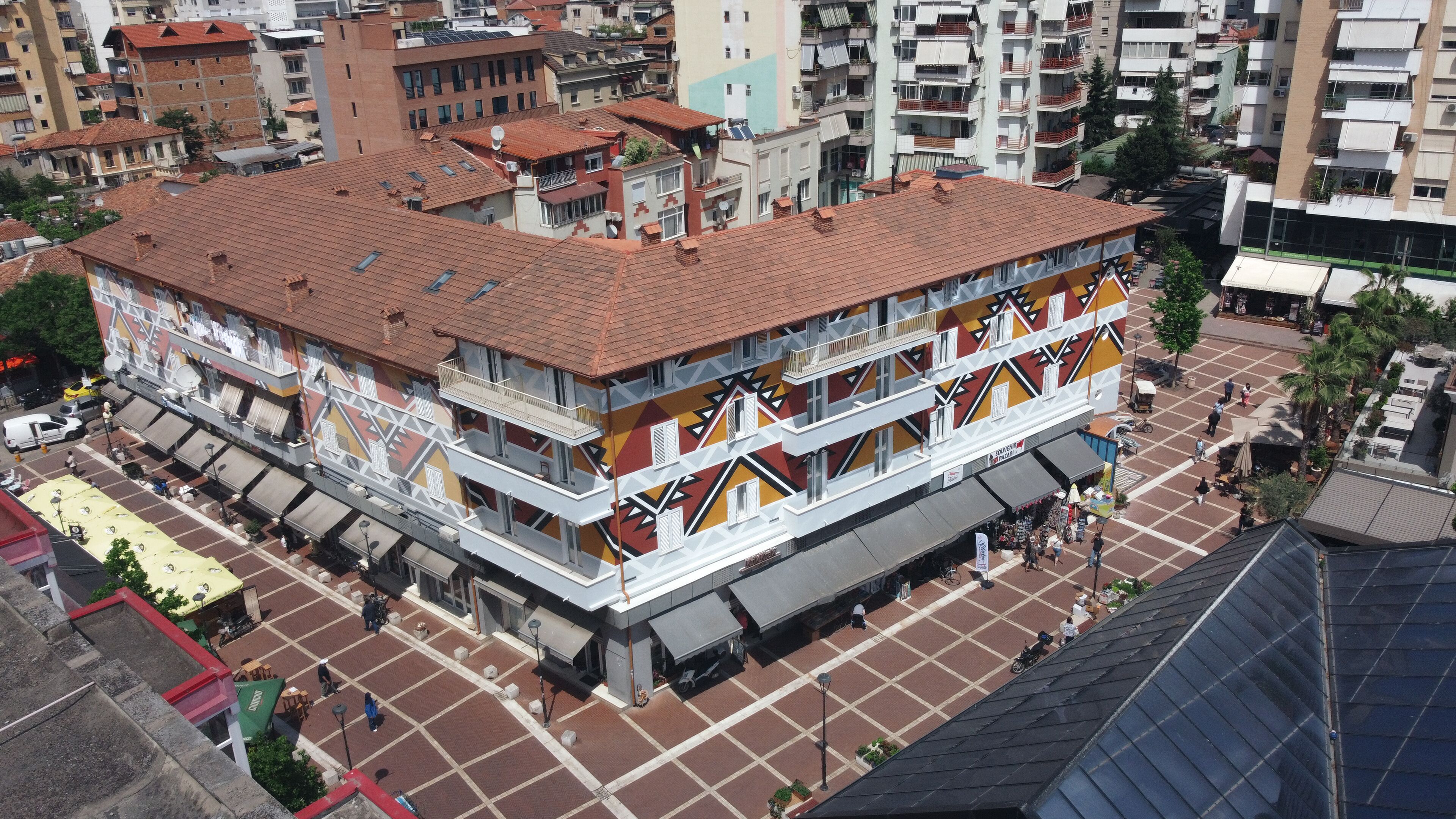 A multi-story building with a tiled roof, a ground floor with a covered outdoor seating area, and a colorful facade with geometric patterns.