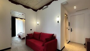 A hotel room with a red sofa, a bed with white bedding, and a door leading to another room. - Bazaar Hotel  (Tirana)