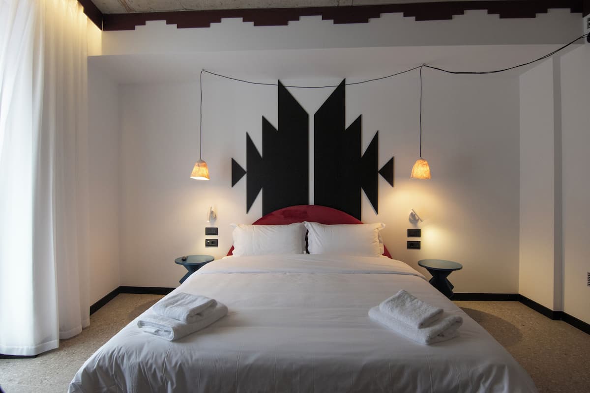 A hotel room with a bed, two bedside tables, a red headboard, and two wall-mounted lamps.