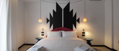 A hotel room with a bed, two bedside tables, a red headboard, and two wall-mounted lamps.