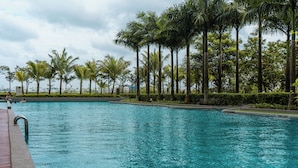 Ein Schwimmbecken mit klarem, blauem Wasser, umgeben von Palmen und einer Hecke.