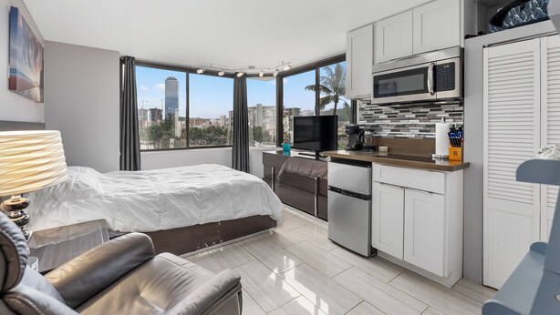 A modern hotel room with a bed, a desk, a kitchenette, and large windows offering a city view. - Canoe Palms Waikiki Pool, Hot Tub, Gym, WiFi, AC (Honolulu)