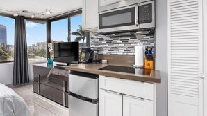 A modern kitchen with a built-in microwave, stove, and dishwasher. It features a large window with a city view and a flat-screen TV. - Canoe Palms Waikiki Pool, Hot Tub, Gym, WiFi, AC (Honolulu)