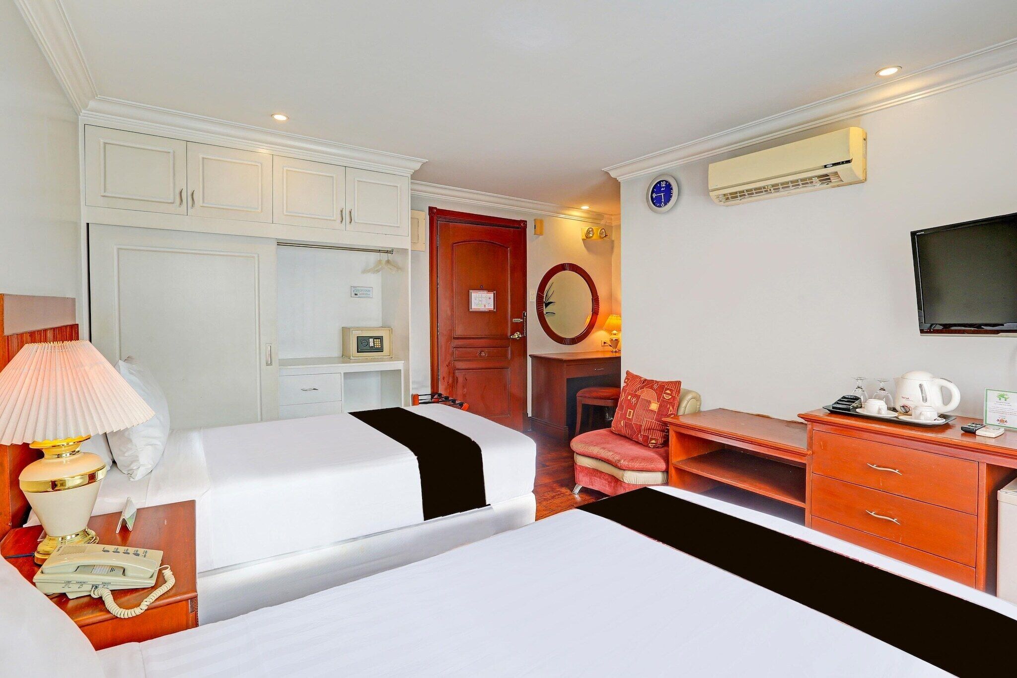 A hotel room with two beds, a desk, a chair, a television, and a wardrobe.