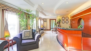 Een hotel lobby met een receptiebalie, zithoek en decoratieve planten.