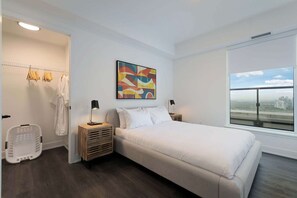 A modern hotel room with a large bed, a city view, a colorful abstract painting, and a laundry area.