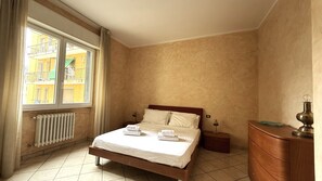 A bedroom with a bed, a radiator, a dresser, and a window with curtains. - Kennedy 2 (Albenga)