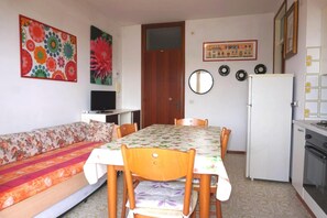 Ein kompakter Wohnbereich mit Sofa, Esstisch, Stühlen, Kühlschrank und einer Küchenzeile.
