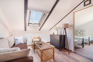 Een slaapkamer in loftstijl met dakraam, een bed, een stoel, een dressoir en een klein tafeltje.
