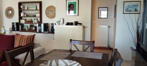 Een woonkamer met een bank, een eettafel, een boekenkast en een radiator.