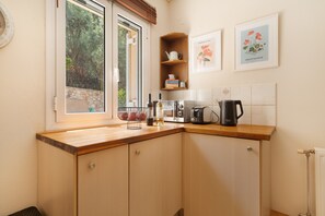 Une cuisine avec des meubles de rangement en bois, un plan de travail, une fenêtre donnant sur des arbres, une étagère contenant des ustensiles de cuisine et des œuvres d’art encadrées accrochées au mur.