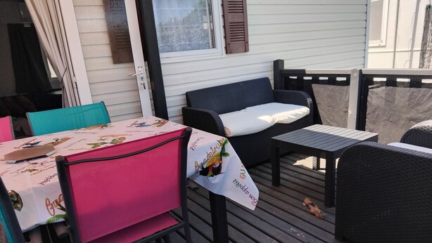 An outdoor patio with a table and chairs, a covered seating area, and a window with shutters. - Mobile home with private parking (Fréjus)