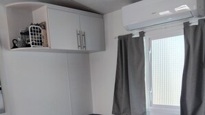 A room with a corner sofa, a small table, a white cabinet, and a window with curtains. - Mobile home with private parking (Fréjus)