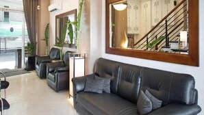Un salon moderne avec un canapé en cuir, une table basse et un grand miroir qui reflète un escalier et un coin repas.
