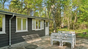 A small building with a porch, white shutters, and a stone patio with white chairs. - Renovated cottage near forest and beach (Rørvig)