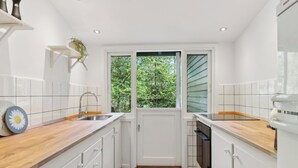 A kitchen with white cabinets, a wooden countertop, a sink, and a view of greenery outside. - Renovated cottage near forest and beach (Rørvig)