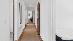 A hallway with a patterned carpet, white walls, and a door leading to a room with a white mattress. - Renovated cottage near forest and beach (Rørvig)