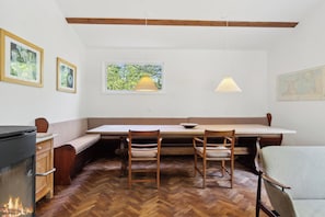 A dining area with a wooden bench, a table, and two chairs. There is a window with a view of greenery, a hanging lamp, and a map on the wall. - Renovated cottage near forest and beach (Rørvig)