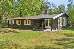 Une maison en bois d’un seul étage, dotée d’un porche couvert, d’une cheminée et d’un petit jardin.