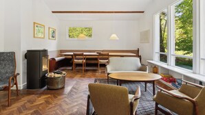 A cozy living room with a fireplace, wooden furniture, and large windows. - Renovated cottage near forest and beach (Rørvig)