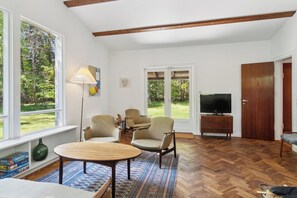 Un salon spacieux doté de grandes fenêtres, d’un parquet en point de Hongrie et d’un téléviseur.