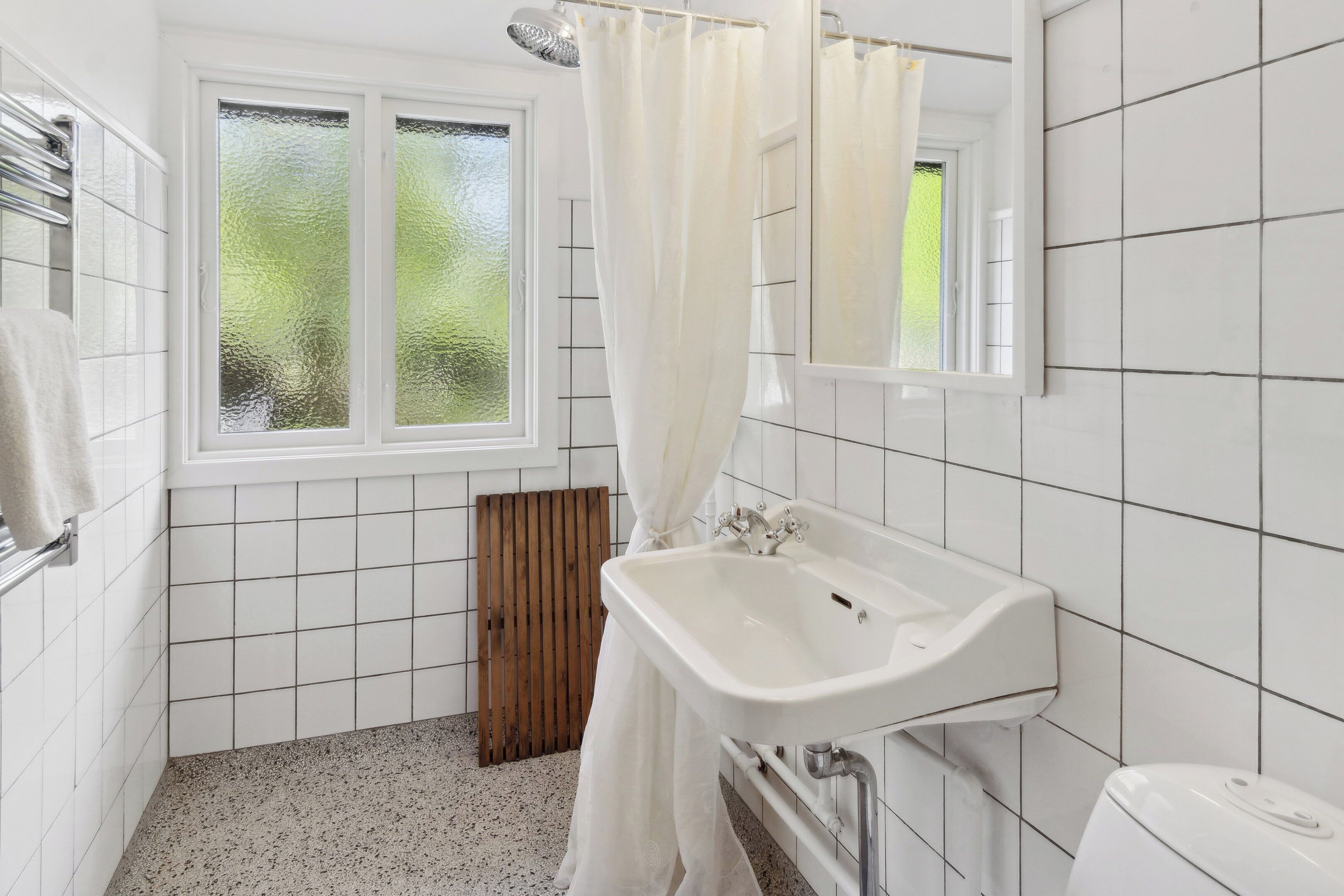 Een badkamer met een wit wastafelmeubel, een douchegordijn, een raam en een spiegel.