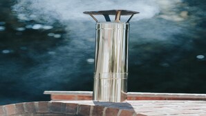 Una parrilla de acero inoxidable para exteriores con chimenea, ubicada sobre un repisa de ladrillo.