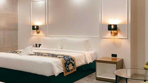 Una habitación de hotel moderna con una cama grande, dos lámparas fijadas a la pared, una mesita auxiliar pequeña y una mesa de vidrio.