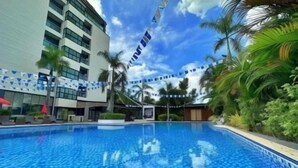 Una piscina con agua azul cristalina, rodeada de palmeras y un edificio moderno con balcones.
