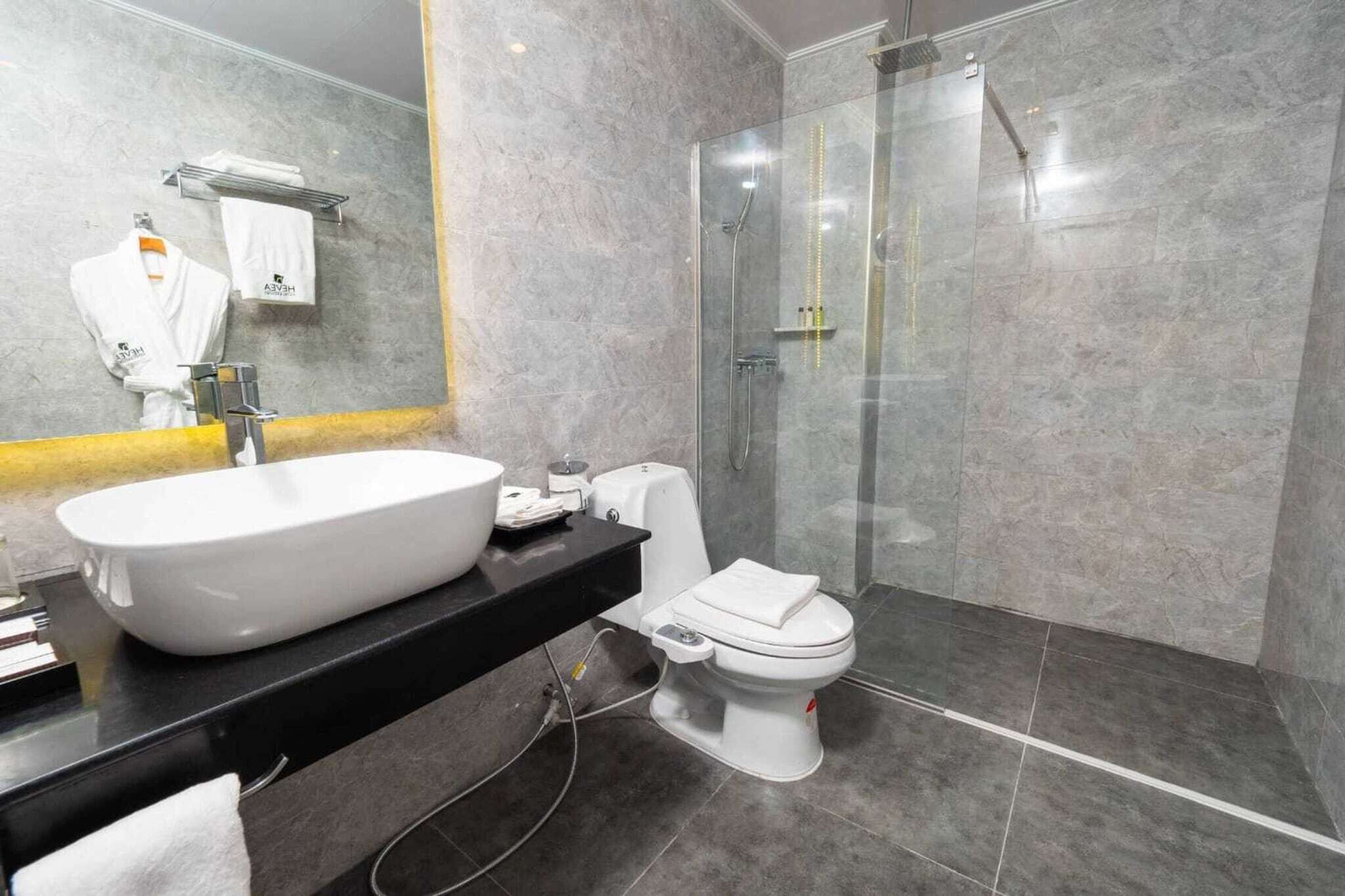 Un baño moderno con un lavamanos grande de color blanco, un inodoro y una cabina de ducha con paredes de vidrio.