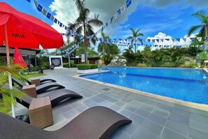 A poolside area with lounge chairs, a red umbrella, and a tropical setting with palm trees.