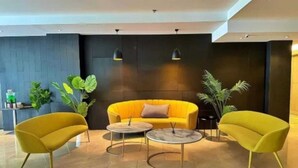 Een moderne lobby met een gele bank, twee bijpassende fauteuils en twee ronde tafels.