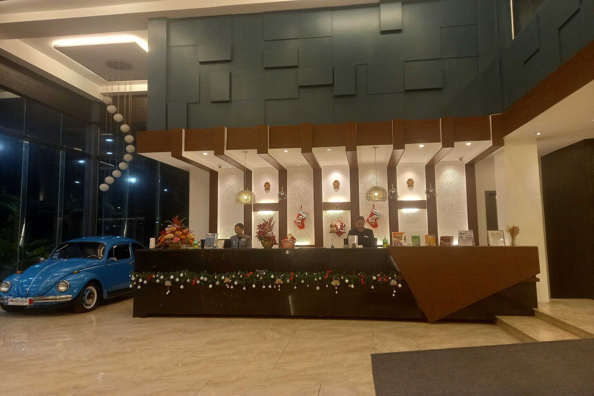 Zona de recepción con diseño moderno, que incluye un mostrador de recepción, luces decorativas y un coche azul estacionado afuera.