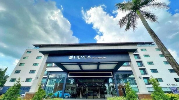 Una entrada de hotel moderna con fachada de vidrio, palmeras y cielo despejado.