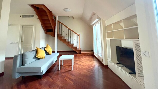 Un salon moderne avec un canapé gris, un escalier en bois et un téléviseur fixé au mur.