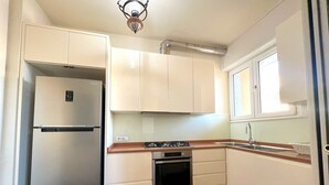 Une cuisine compacte avec des meubles blancs, un réfrigérateur en acier inoxydable, une cuisinière à gaz et un four encastré.