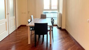 Une pièce spacieuse avec un plancher en bois, une table à manger blanche et quatre chaises, une fenêtre donnant sur un beau paysage et un radiateur.