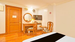 Hotellihuone, jossa on puinen ovi, peilillä varustettu työpöytä, televisio, pieni pöytä, kaksi tuolia ja sänky.