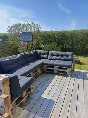 Een modulaire bank op een houten terras, met een basketbalveld op de achtergrond.