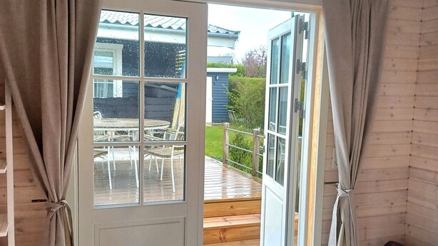 A room with a bed, a window with curtains, a view of an outdoor deck, and a radiator. - Lovely cottage close to the water (Karrebæksminde)