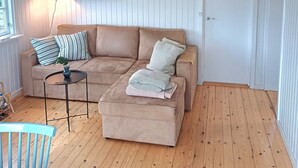 A room with a wooden floor, a beige sofa, a small table, a chair, and a door. - Lovely cottage close to the water (Karrebæksminde)