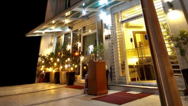 A hotel entrance with a covered outdoor area, potted plants, and a staircase leading inside.