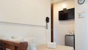 A single bed with a wooden headboard, a bedside telephone, a small refrigerator, and a mounted television on the wall.