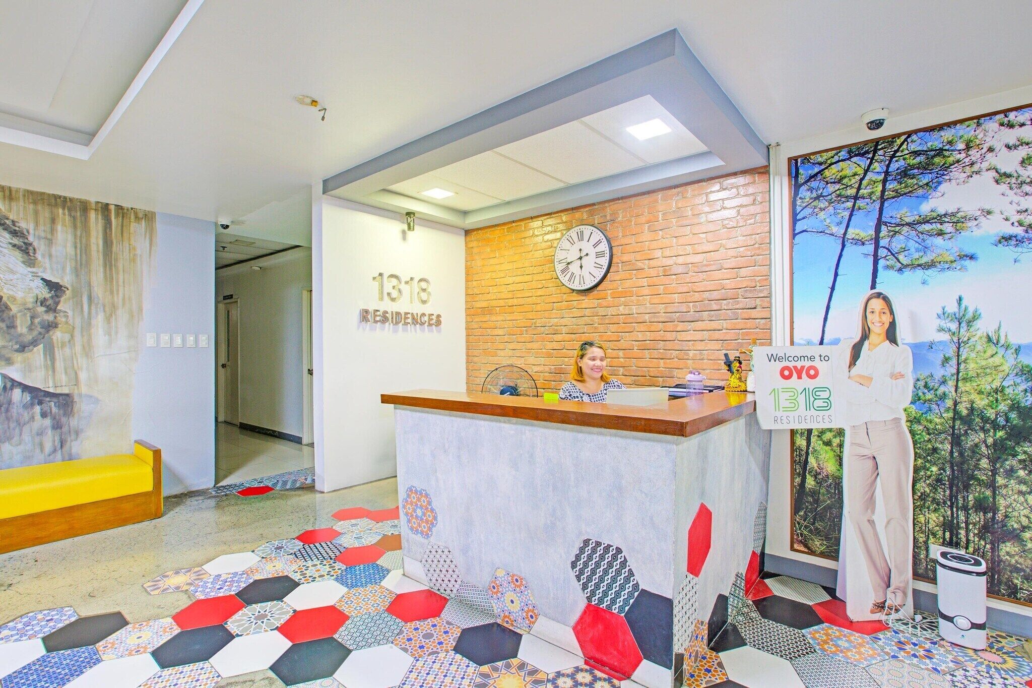 A reception area with a brick wall, a clock, a colorful geometric floor pattern, and a large window with a forest view.
