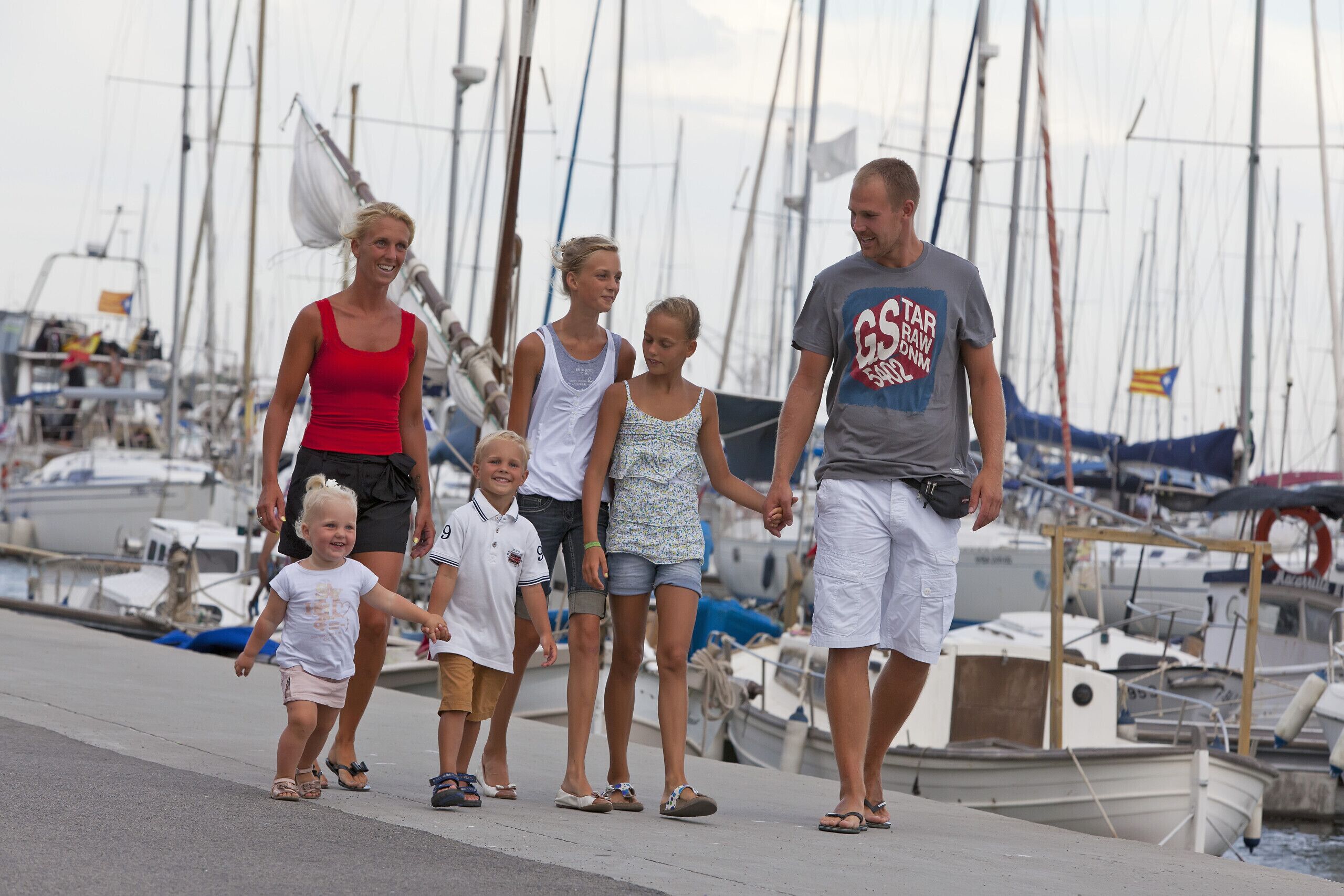 A family walking along a pier with boats in the background.