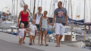Una familia caminando por un muelle con barcos al fondo.