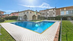 Piscina con borde de baldosas, rodeada por una valla y follaje.