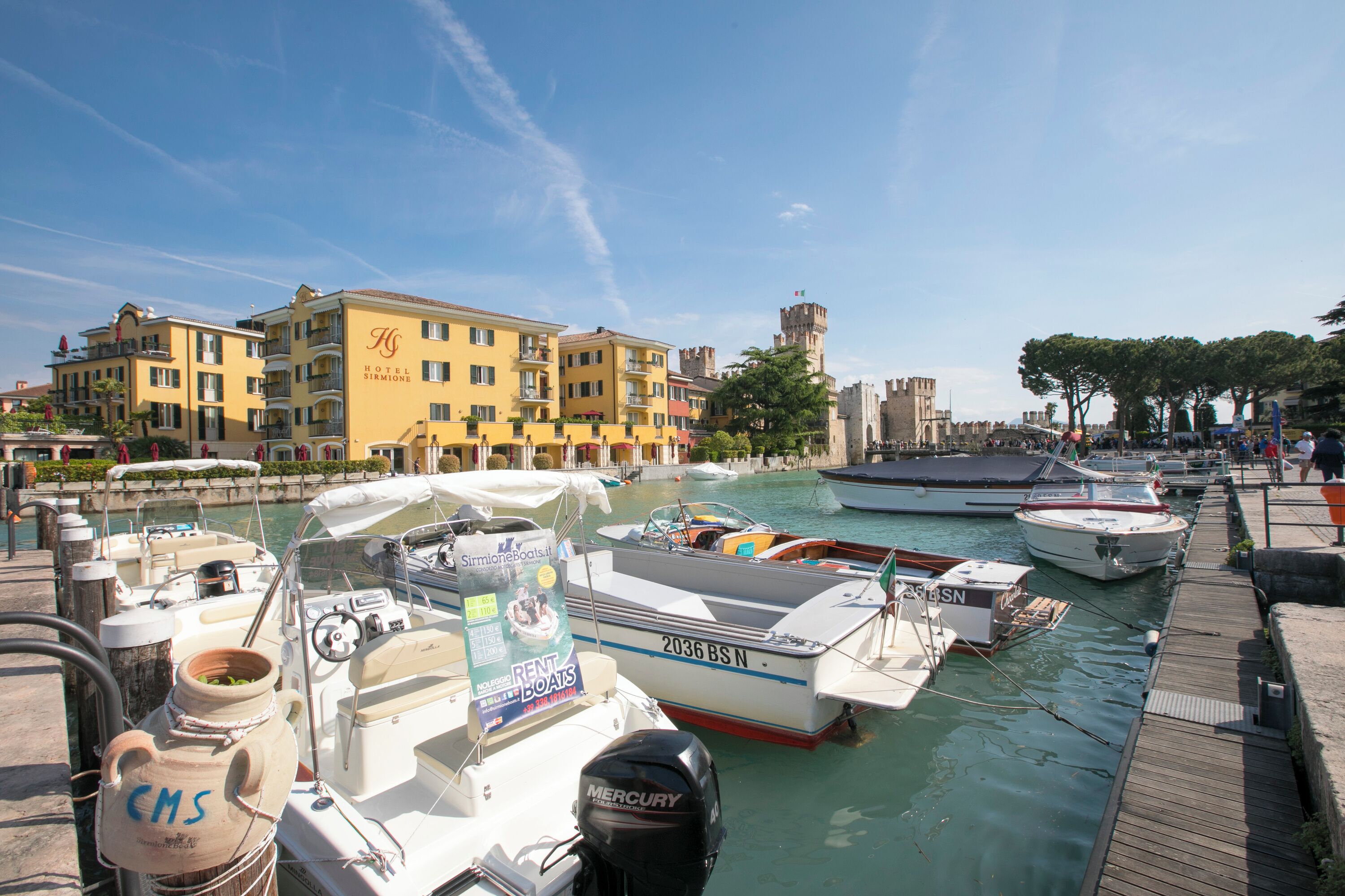A marina with boats docked, a yellow building with balconies, and a tower in the background.